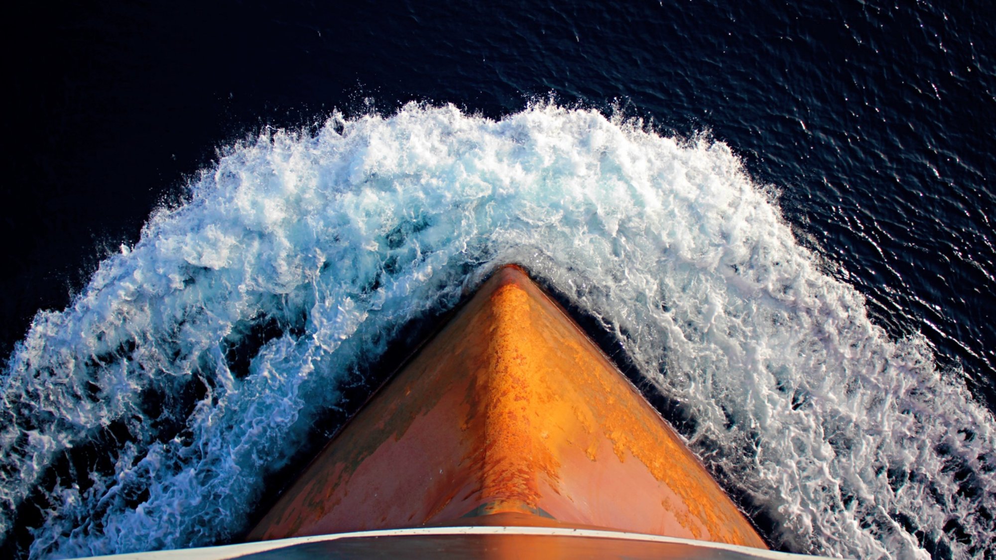 Aerial photograph of a ship's orange bow cutting through deep blue water
